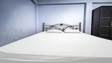 Un letto singolo con testiera in metallo in una stanza dalle pareti spoglie e un armadio scuro.