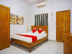 A bedroom with a wooden bed, a white mattress, red and white pillows, a grey curtain, and a wooden wardrobe. - Oyo 91456 Anggrek Homes Makassar (Makassar)