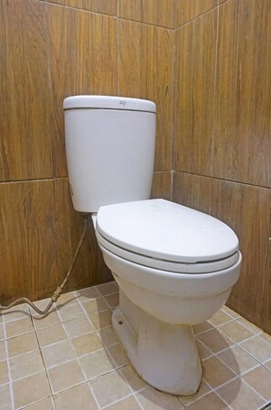 A white toilet in a bathroom with wooden panel walls and tiled floor. - Oyo 91456 Anggrek Homes Makassar (Makassar)