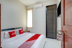 Habitación de hotel con cama, unidad de aire acondicionado, ventana con cortinas y puerta con letrero de 'No molestar'.