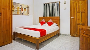 Un dormitorio con una cama de madera, colchón blanco, almohadas rojas y blancas, cortina gris y un armario de madera.