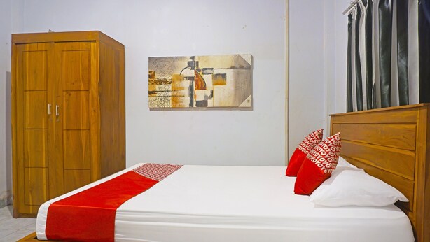 Una cama bien hecha con una colcha roja y blanca, un cabecero de madera y una sola almohada roja.
