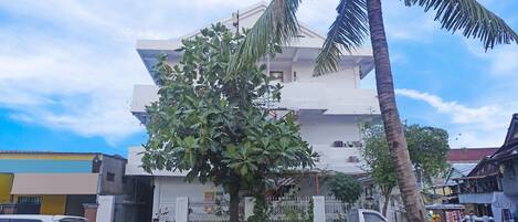 A multi-story building with a white exterior, a tree in front, and a parked white car.