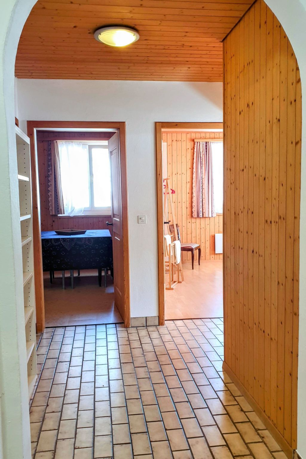 A room with a tiled floor, a wooden ceiling, a window with curtains, and a dining area with a table and chairs.
