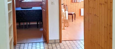 Une pièce avec un sol carrelé, un plafond en bois, une fenêtre avec des rideaux et un coin repas comprenant une table et des chaises.