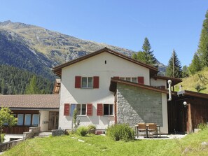 A two-story building with a stone facade and red shutters, set against a mountainous backdrop. - Starlera, (Innerferrera), by Interhome (Innerferrera)