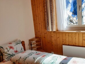 A room with wooden walls, a bed with floral bedding, a chair, and a window with curtains.