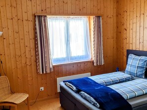 A wooden-paneled room with a bed, a chair, and a window with curtains. - Starlera, (Innerferrera), by Interhome (Innerferrera)