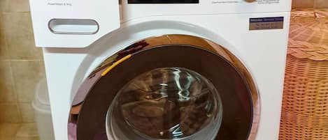 A white Miele washing machine with a control panel, a door, and a hose.