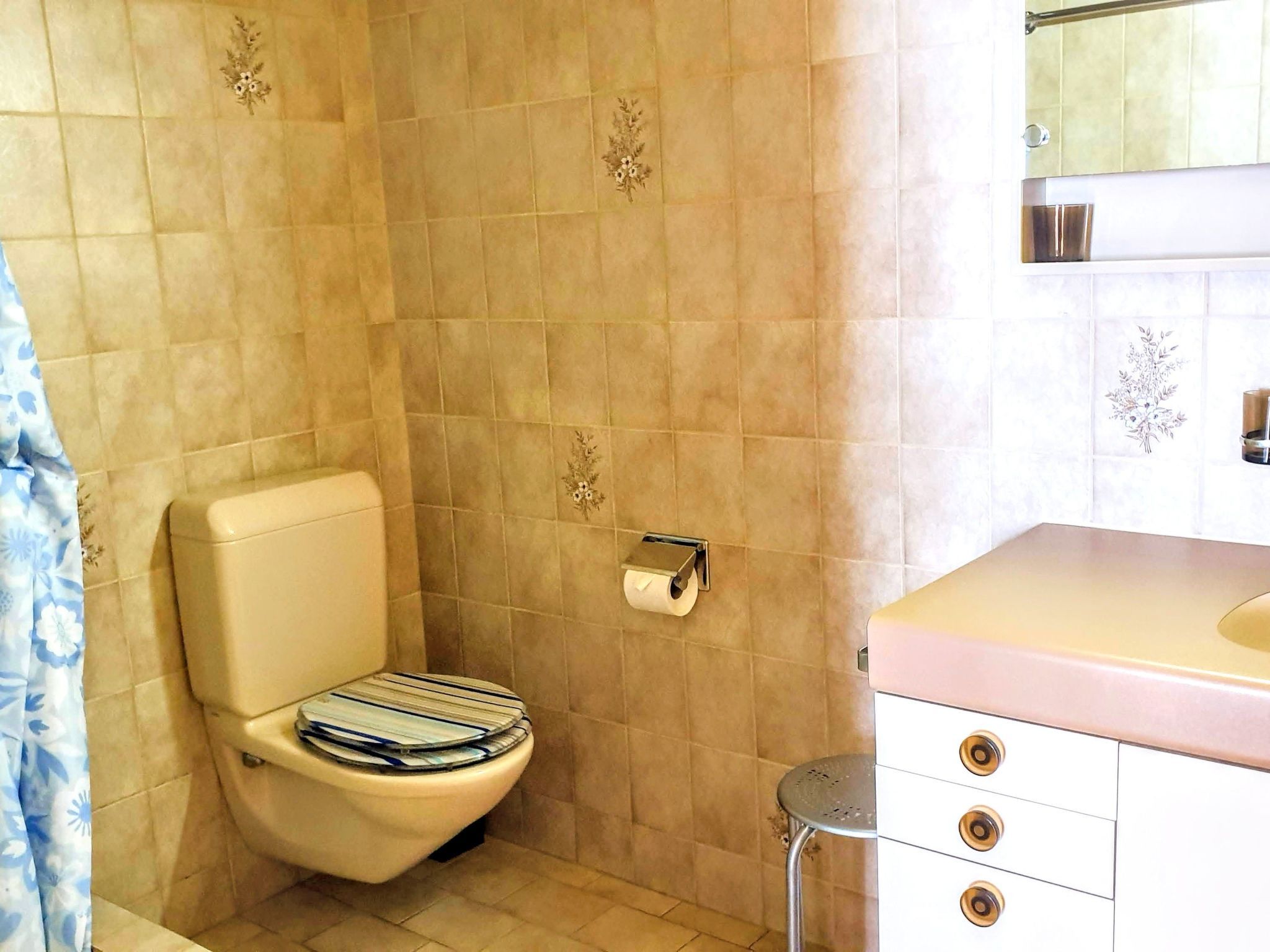 A bathroom with a toilet, a roll of toilet paper, a sink with a mirror, and a shower area.