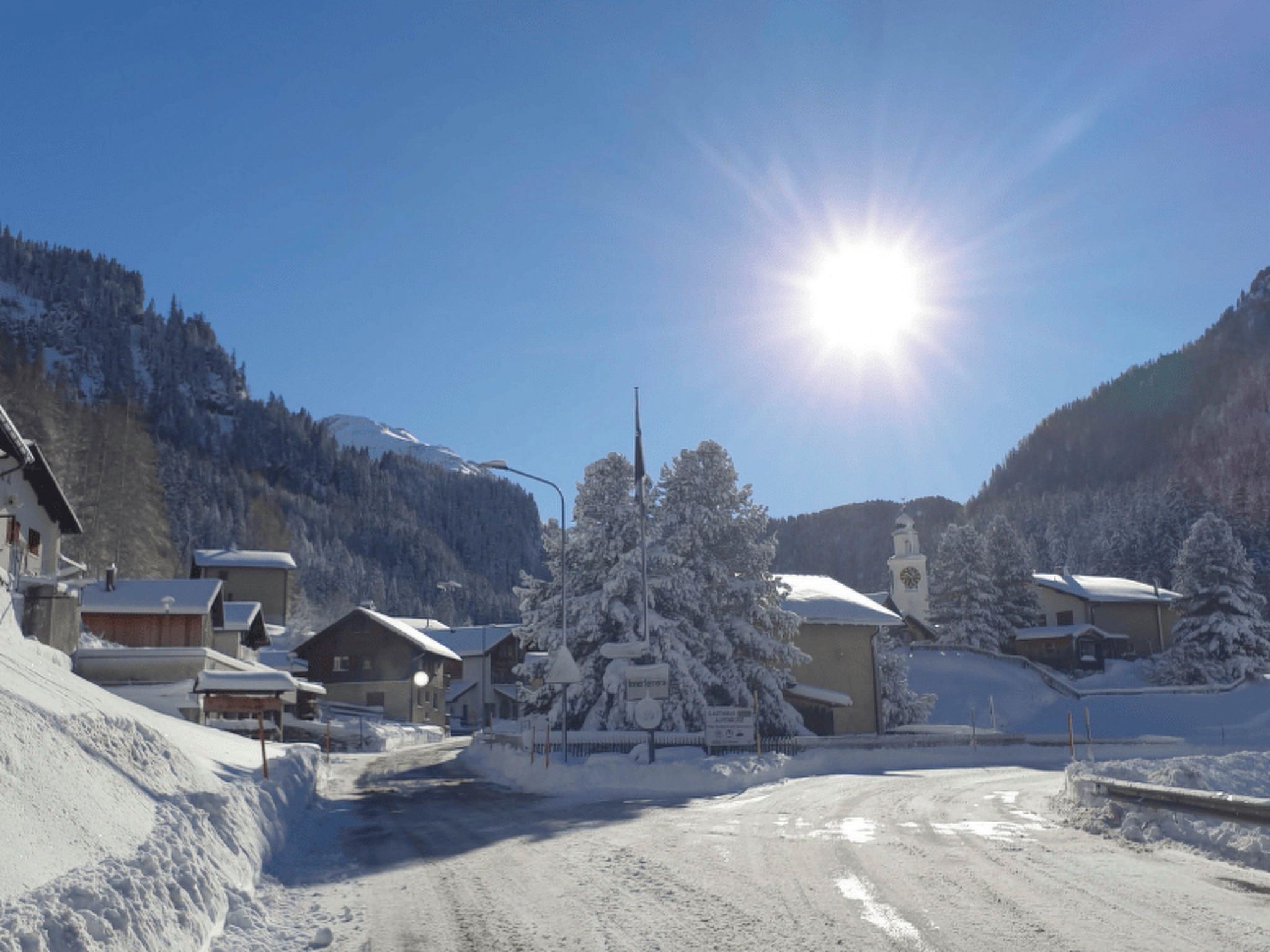 En snötäckt by med traditionella byggnader, en klar himmel och en strålande sol.