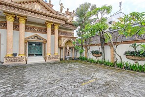 A courtyard with a traditional building featuring ornate columns and statues, a paved walkway, and potted plants. - Hotel Srikandi Kalasan (Kalasan)