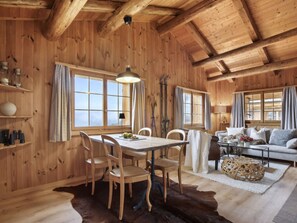 Interior de una cabaña de madera con una mesa de comedor, sillas, un sofá y una chimenea.