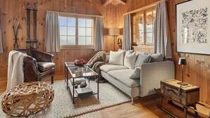 Ein Zimmer mit Holzwänden, einem Ledersessel, einem Sofa, einem Glastisch und einem gerahmten Bild an der Wand.