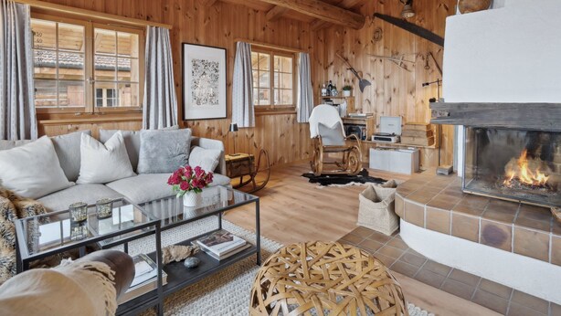 Ein gemütliches Blockhaus-Interieur mit Kamin, Holzwänden, einer Couch, einem Schaukelstuhl und einem Esstisch.