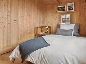 Una habitación de madera con una cama, una mesita de noche, una ventana y dos cuadros en la pared.