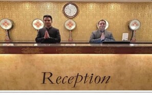 A reception desk with a 'Reception' sign, two individuals standing behind it, and decorative wall clocks. - The Fern Denzong Hotel And Spa, Gantok (Gangtok)