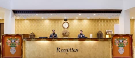 Un mostrador de recepción con un reloj, dos empleados y un letrero que dice 'Reception'.