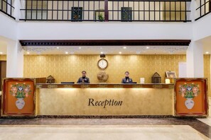 Un mostrador de recepción con un reloj, dos empleados y un letrero que dice 'Reception'.