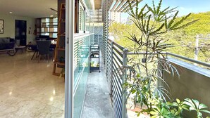 Un couloir doté d’une rambarde en verre, qui mène à un balcon agrémenté de plantes et offrant une vue sur la ville.
