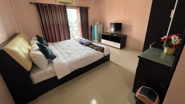 Un dormitorio con cama, televisor, armario y una pequeña mesa con flores.