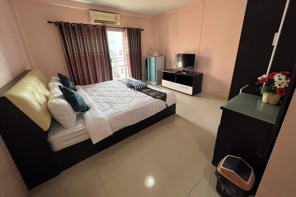 A bedroom with a bed, a TV, a wardrobe, and a small table with flowers.
