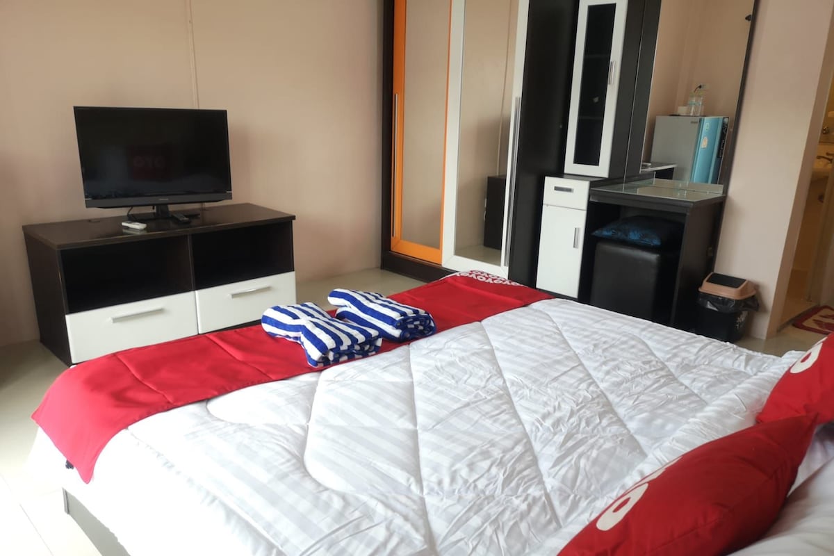 A hotel room with a bed, a TV on a black cabinet, a wardrobe, and a mirror.