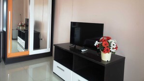 Una habitación moderna con un espejo grande, un televisor de pantalla plana sobre un soporte negro, y una planta en maceta con flores rojas y blancas.