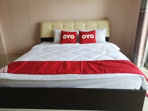 A bed with a white and red bedspread, two red pillows with "OYO" text, and a cream-colored headboard. - Oyo 75414 Kjs Pattaya (Pattaya)