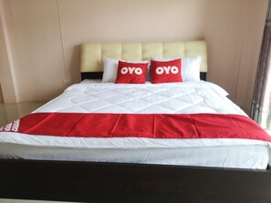 Sängyssä on valkoinen ja punainen päiväpeite, kaksi punaista tyynyä, joissa on teksti ”OYO”, ja kermanvärinen pääty.