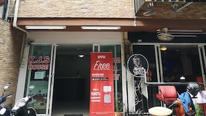 Un edificio de varios pisos con balcones, un letrero con la inscripción K.J.S HOUSE y un cartel que anuncia un cupón de descuento del 100%.