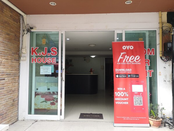 A hotel entrance with a K.J.S House sign, a red promotional sign for the OYO app, and a welcome mat. - Oyo 75414 Kjs Pattaya (Pattaya)
