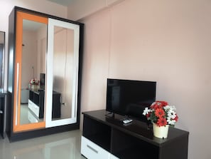 A modern room with a large wardrobe, a flat-screen TV on a black stand, and a potted plant with red and white flowers. - Oyo 75414 Kjs Pattaya (Pattaya)