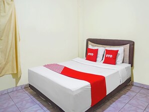 Un letto con una coperta bianca e rossa, due cuscini rossi con il testo 'OYO' e un poggiatesta marrone.