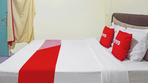 A bed with a white and red bedspread, two red pillows with 'YOYO' text, and a yellow curtain. - Oyo 91766 Fortuna Hotel Syariah (Banyumas)