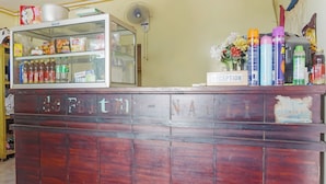 A reception desk with a glass display case containing snacks and beverages, a fan, and a 'RECEPTION' sign. - Oyo 91766 Fortuna Hotel Syariah (Banyumas)