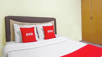 A bed with a white and red bedspread, two red pillows with 'OYO' text, a brown upholstered headboard, and a wooden wardrobe.