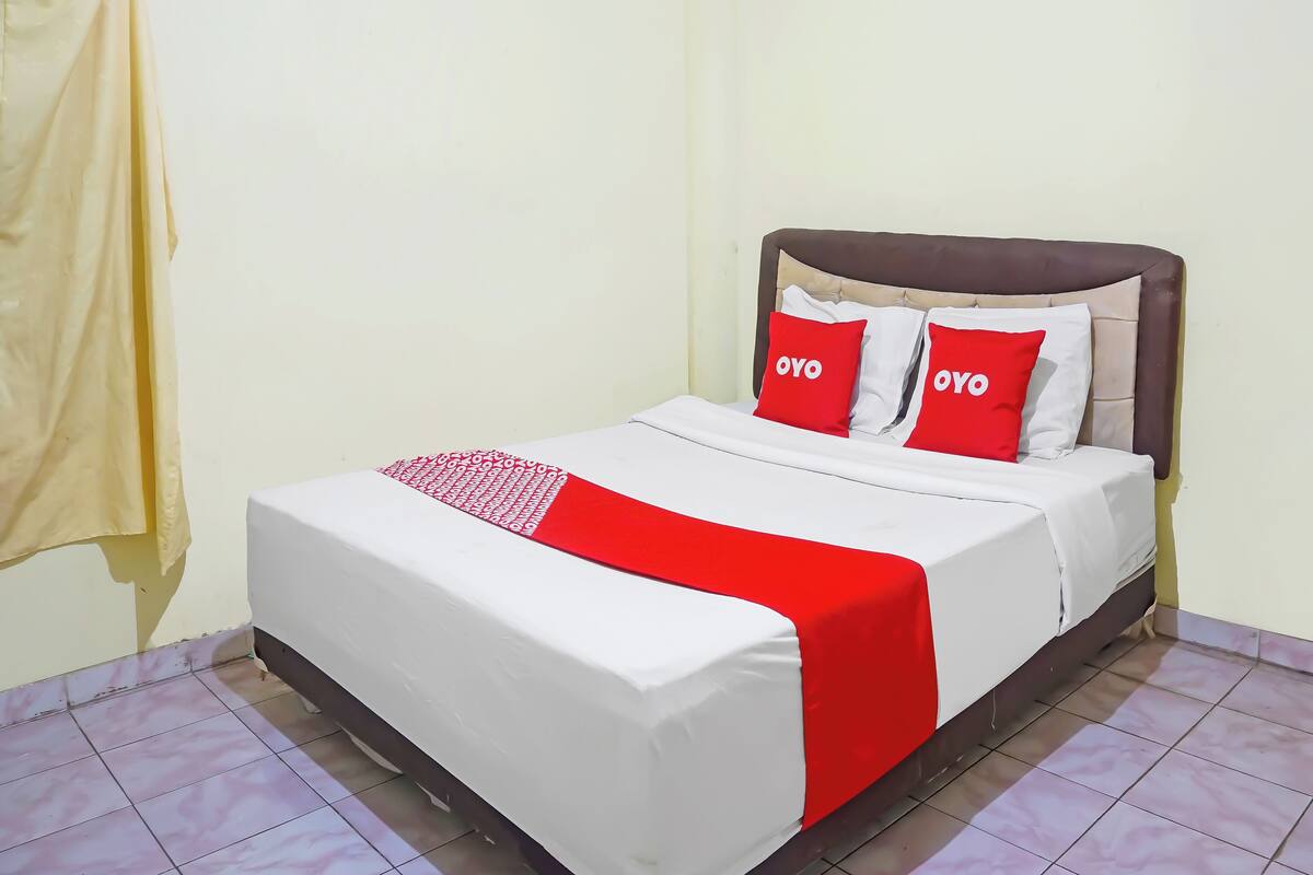 Een bed met een wit en rood dekbed, twee rode kussens met de tekst 'OYO' en een bruin hoofdeinde.
