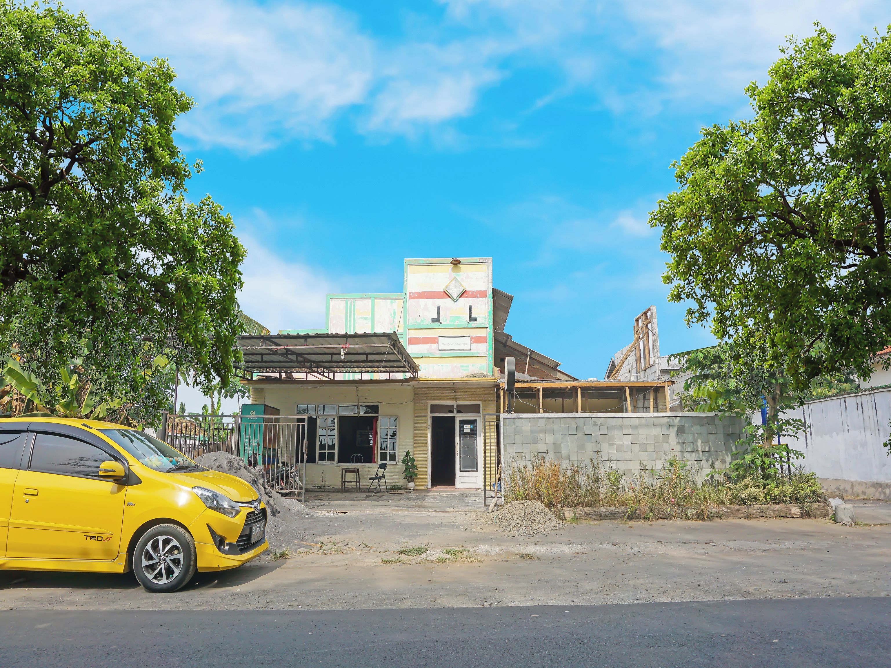 A building with a large sign, a yellow car parked in front, and trees around.