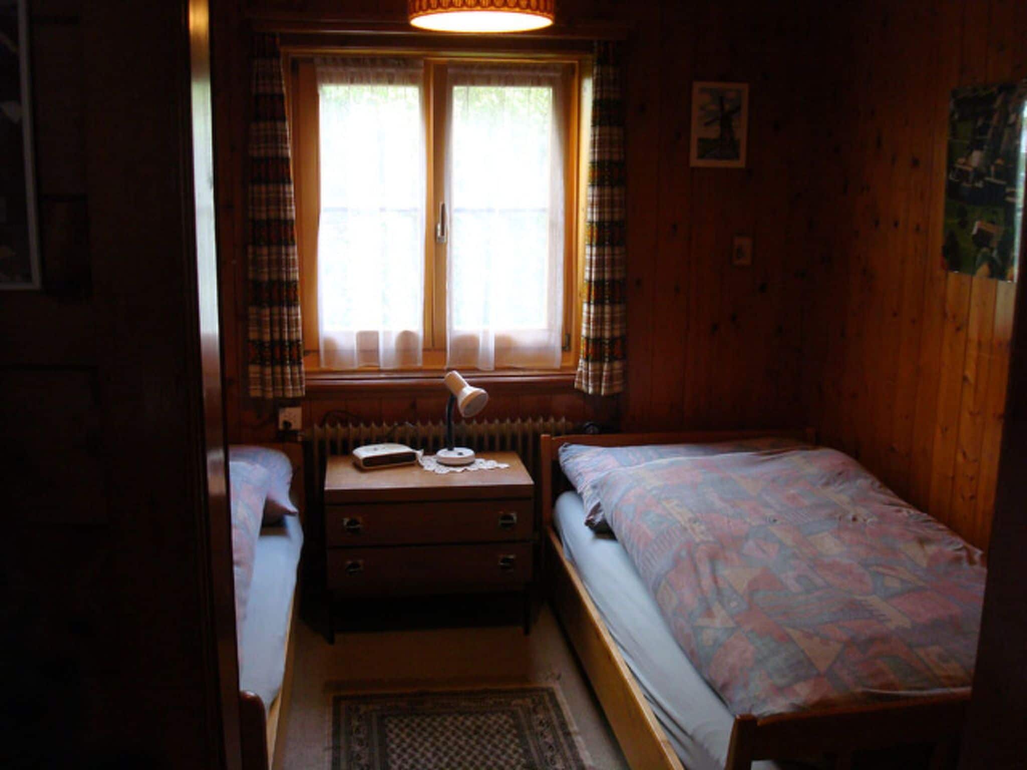 Een kleine, knusse kamer met een bed, een dressoir, een bureau en een raam met gordijnen.