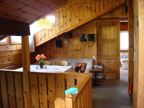 Interno di una baita in legno con angolo pranzo, divano e una scala.
