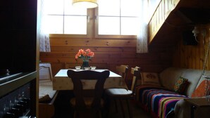 A wooden cabin interior with a dining table, chairs, a sofa, and a window with curtains. - Haus Vernier, (Seewis). by Interhome (Seewis im Prättigau)