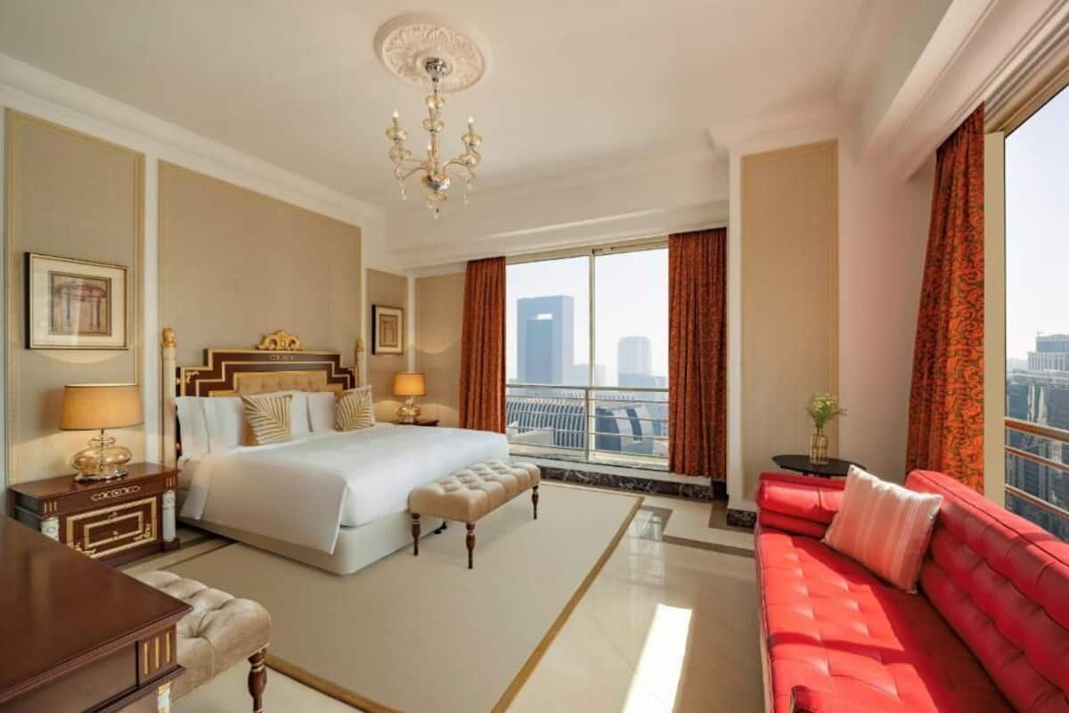 Ein Hotelzimmer mit einem großen Bett, einem roten Sofa, einer Kristallleuchter und Blick auf die Stadt.
