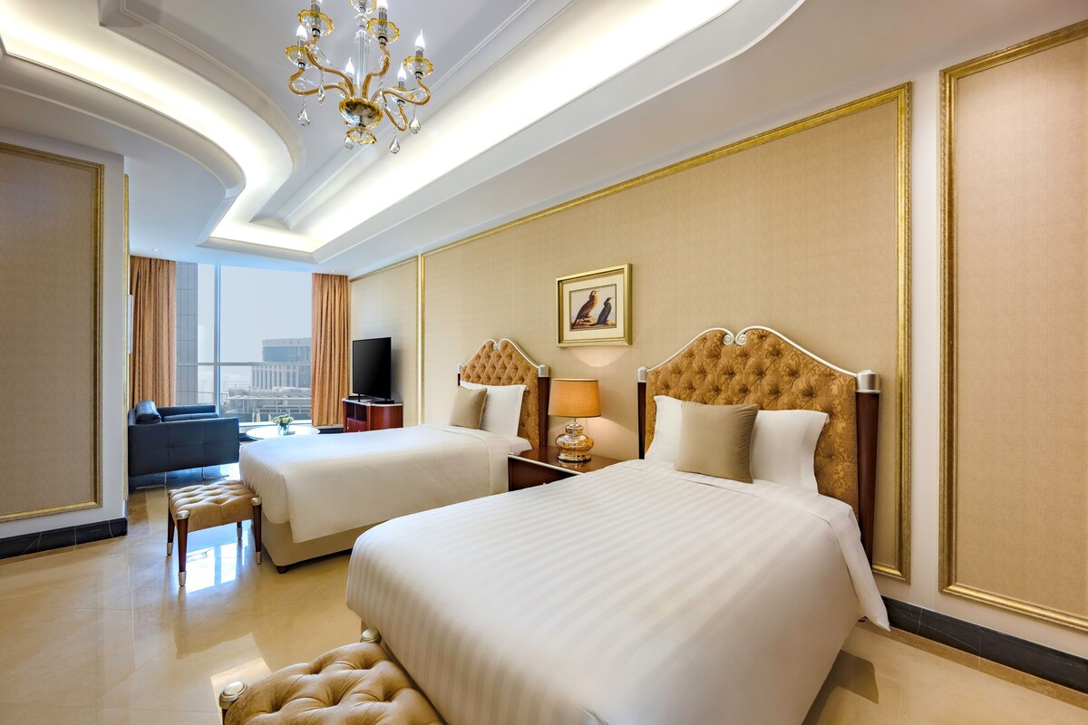 A hotel room with two beds, a TV, a sofa, and a view of the city.