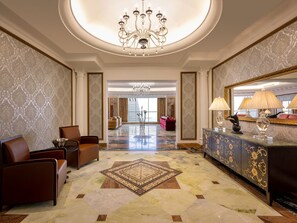 A spacious lobby with a chandelier, a seating area with leather chairs, a decorative console table with lamps, and a large mirror. - Dusit Hotel and Suites Doha (Doha)