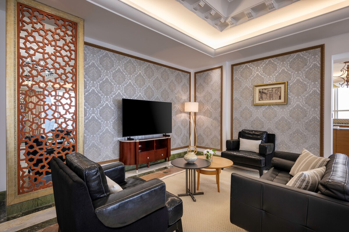 A modern living room with a flat-screen TV, leather sofas, a coffee table, and a decorative wall panel.