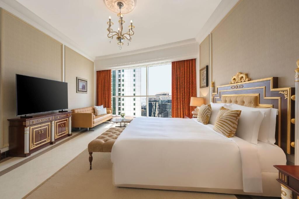 A spacious hotel room with a large bed, a television, a seating area, and a view of the cityscape.