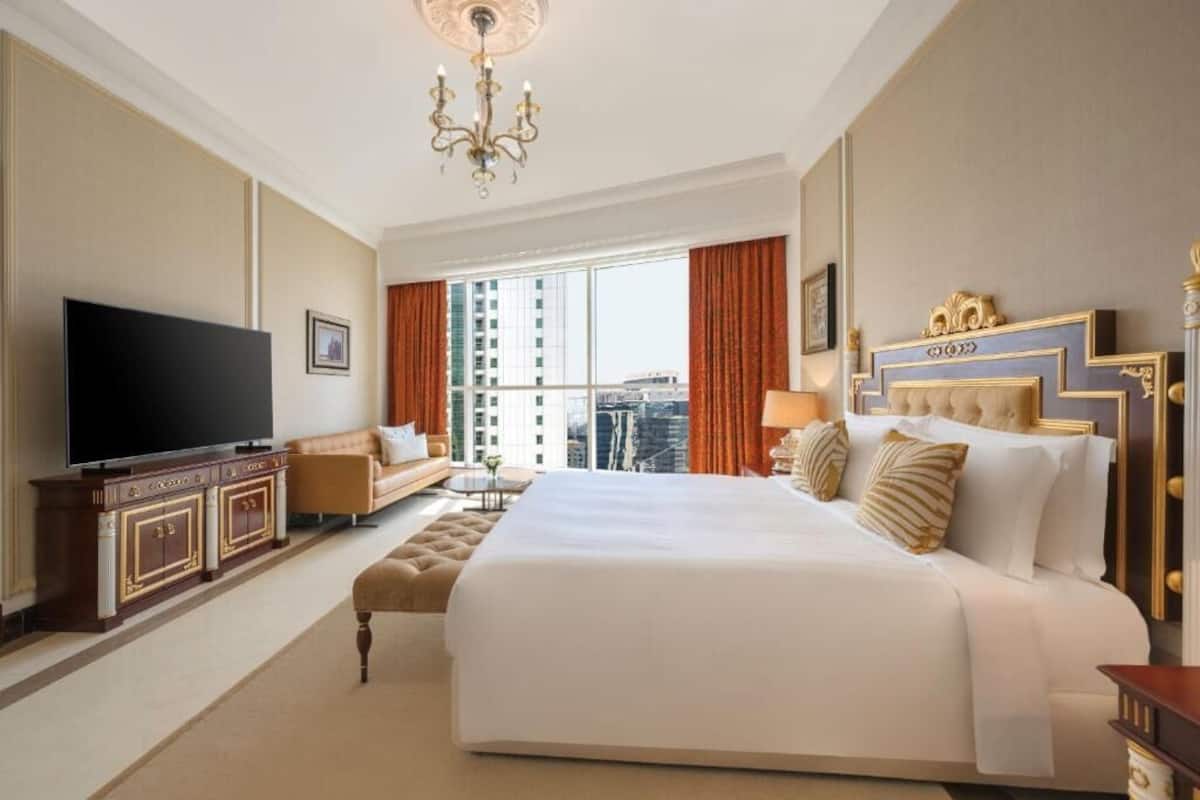 Ein geräumiges Hotelzimmer mit einem großen Bett, einem Fernseher, einer Sitzecke und Blick auf die Stadt.