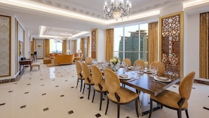 A spacious dining area with a long table set for a meal, surrounded by chairs, a chandelier, and large windows. - Dusit Hotel and Suites Doha (Doha)