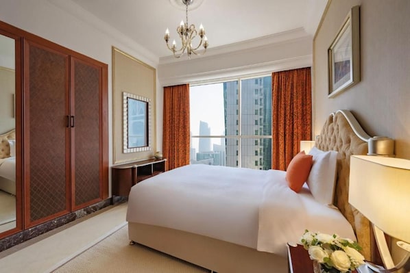 A hotel room with a large bed, a wardrobe, a desk, and a view of the city. - Dusit Hotel and Suites Doha (Doha)